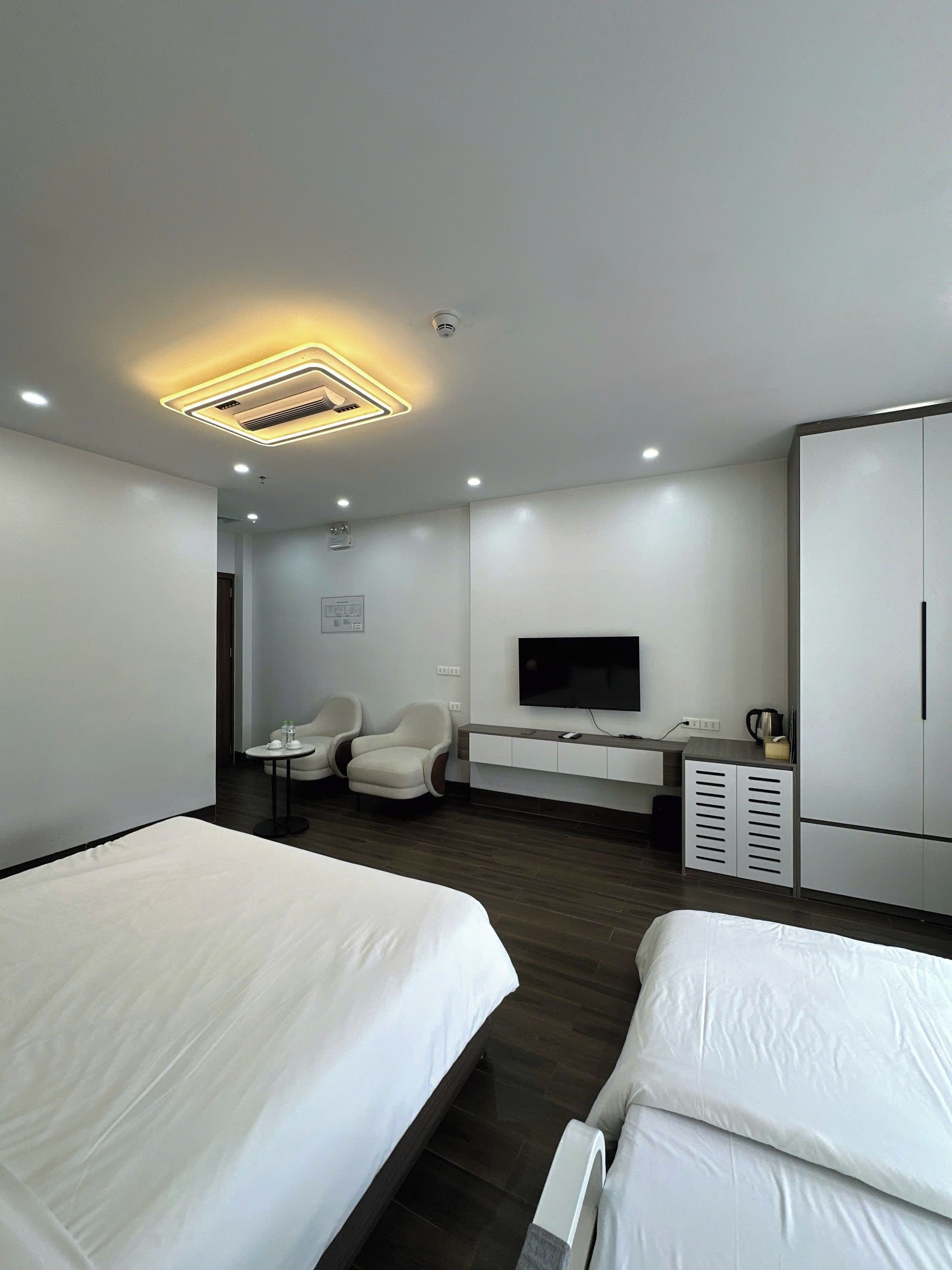 Ein modernes Hotelzimmer mit einem großen Bett, einem Schreibtisch mit Flachbildfernseher, einer Sitzecke mit zwei Stühlen und einem Kleiderschrank.