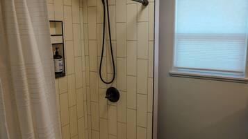A walk-in shower with a glass door, a towel rack, and a window with blinds.