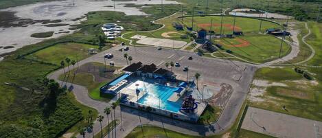 An aerial view of a sports complex with a swimming pool, baseball fields, and parking areas.