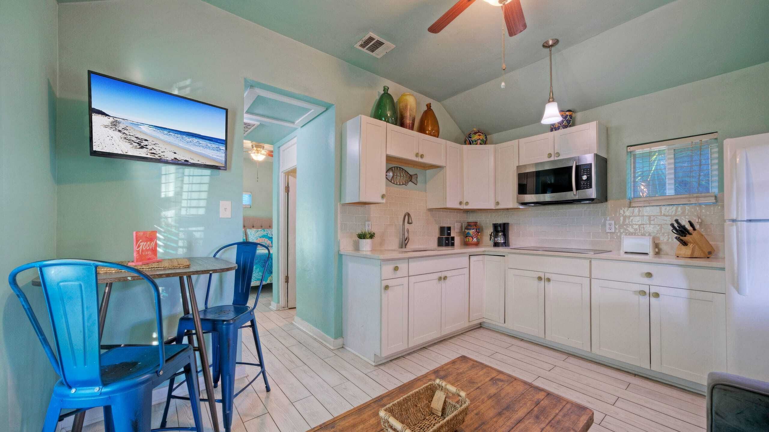 A kitchen with white cabinets, a microwave, and a TV displaying a beach scene.