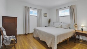 A bedroom with a bed, a nightstand, a lamp, a chair, a wardrobe, and two windows with curtains. - Beautiful 2-bedroom apartment with AC in vibrant Columbus (Columbus)