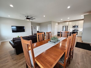 A spacious living room with a wooden dining table, leather sofa, and a ceiling fan.