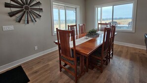 A dining room with a wooden table and chairs, large windows, and a decorative metal wall piece. - Modern home on acreage with pond, trails, rolling hills, and sunset views (Winterset)
