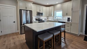 A modern kitchen with white cabinets, stainless steel appliances, and a large island with bar stools. - Modern home on acreage with pond, trails, rolling hills, and sunset views (Winterset)