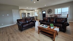 A spacious living room with two leather sofas, a wooden coffee table, and a ceiling fan. - Modern home on acreage with pond, trails, rolling hills, and sunset views (Winterset)