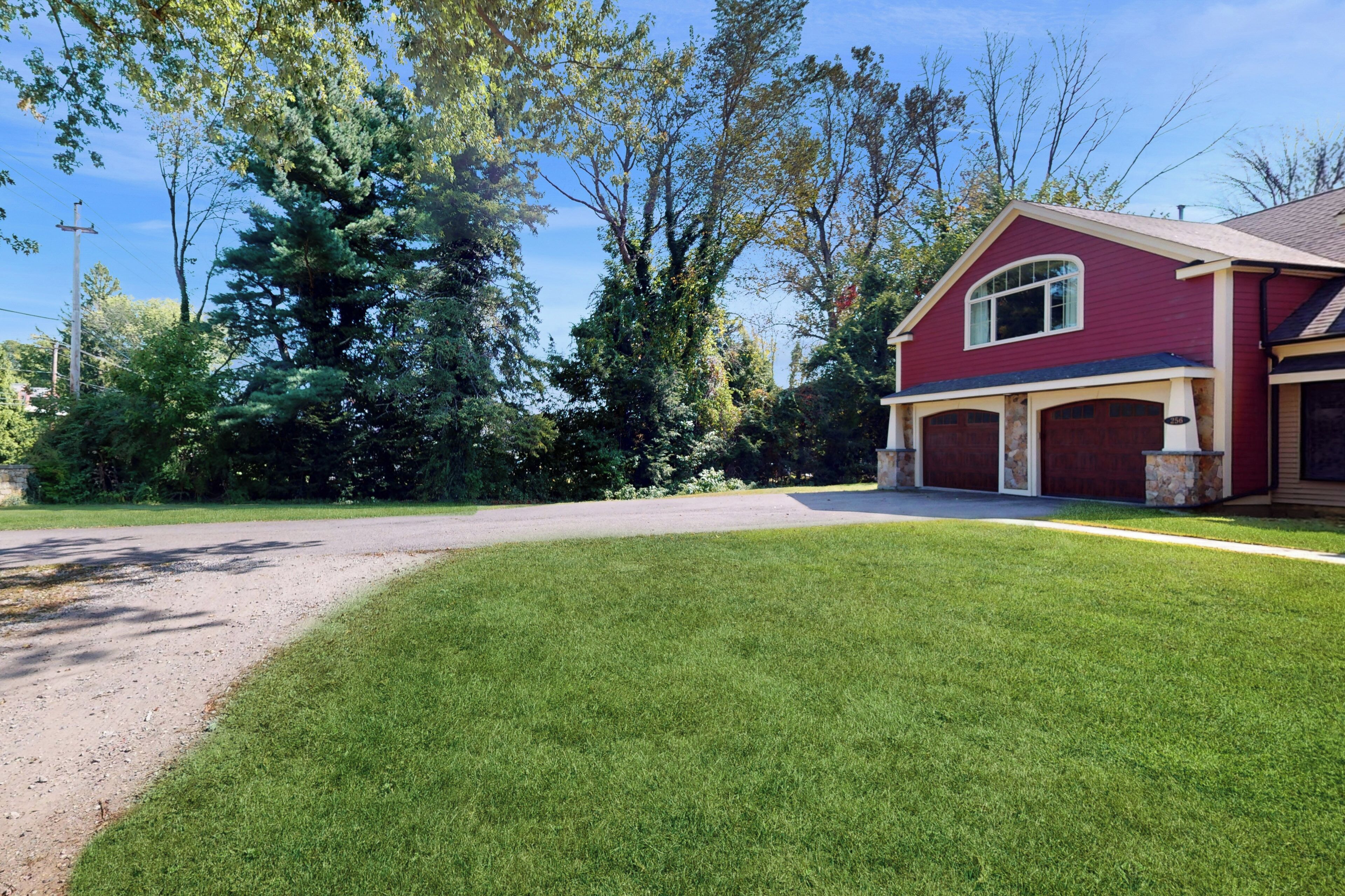 Une maison rouge avec un garage, entourée d’une pelouse bien entretenue et d’arbres.