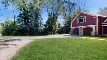 Une maison rouge avec un garage, entourée d’une pelouse bien entretenue et d’arbres.