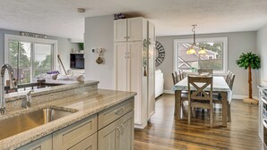 A kitchen with granite countertops, a sink, cabinets, a dining table with chairs, a clock, and a plant. - Coastal York Gem Near Beach: Work, Play & Explore! (York)