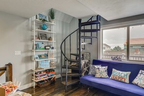 A living room with a blue sofa, a white bookshelf, and a spiral staircase. - Coastal York Gem Near Beach: Work, Play & Explore! (York)