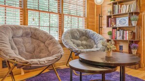 Una habitación acogedora con dos sillones grandes y mullidos, una mesa redonda y una estantería llena de libros y plantas.
