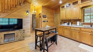 Un interior de madera con una escalera, un televisor, una mesa de madera con bancos y una zona de cocina con armarios de madera y un lavamanos.