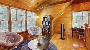 Una cabaña de madera acogedora con ventanas amplias, un sillón cómodo, una estantería y un escritorio.