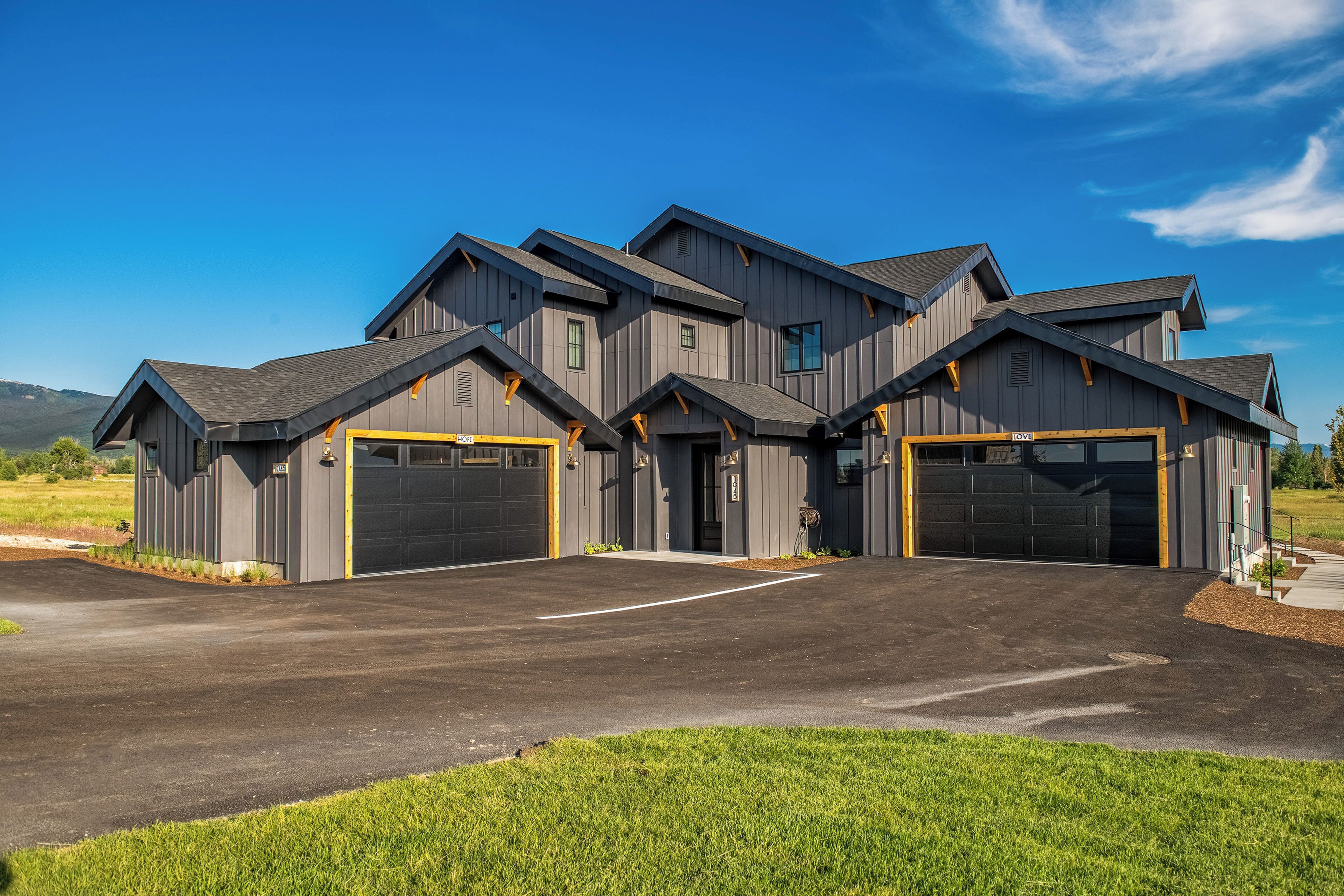 A modern multi-story building with two garage doors and a driveway.