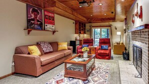 A cozy living room with a wooden ceiling, a fireplace, a red armchair, and a sofa with a 'HOME' pillow. - Salisbury Waterfront: Schumaker Pond Paradise! (Salisbury)