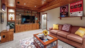 A cozy living room with a wooden ceiling, a television, a sofa with patterned cushions, and a coffee table with books and a vase. - Salisbury Waterfront: Schumaker Pond Paradise! (Salisbury)