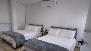 Ein Hotelzimmer mit zwei Betten, einem kleinen Nachttisch, einer Wand-Klimaanlage und einem gemusterten Boden.