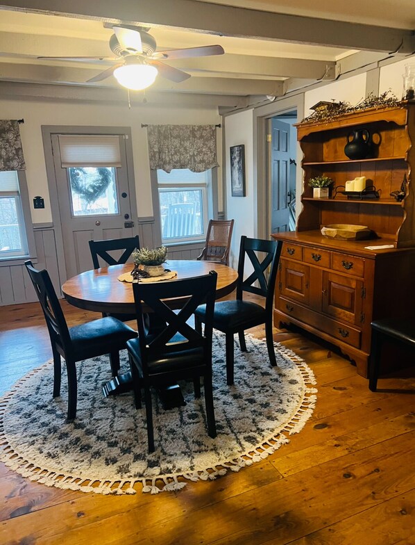 A dining area with a round table, four chairs, a ceiling fan, and a wooden cabinet with shelves.