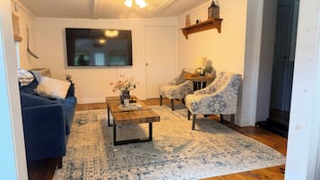 Un salon avec un canapé bleu, des fauteuils à motifs, une table basse et un téléviseur fixé au mur.