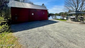 A red building with a metal roof, a gravel driveway, and a gazebo with outdoor seating. - Waterfront 1860s Farmhouse, Private Hot Tub, Fire Pit, Pond, Canoe, Walk to Town (Chestertown)