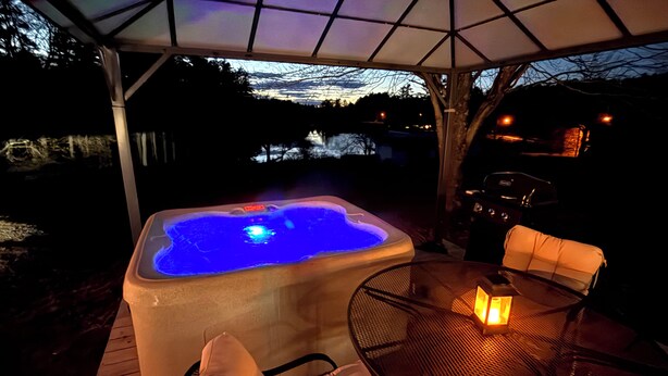 A hot tub under a covered patio with a view of a lake at dusk. - Waterfront 1860s Farmhouse, Private Hot Tub, Fire Pit, Pond, Canoe, Walk to Town (Chestertown)