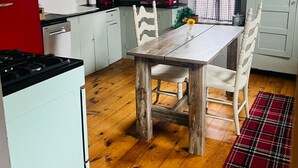 A kitchen with a wooden table and chairs, a red refrigerator, and a window with curtains. - Waterfront 1860s Farmhouse, Private Hot Tub, Fire Pit, Pond, Canoe, Walk to Town (Chestertown)