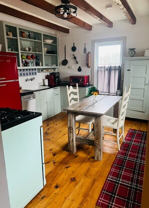 A kitchen with a wooden table and chairs, a red refrigerator, and a window with curtains.