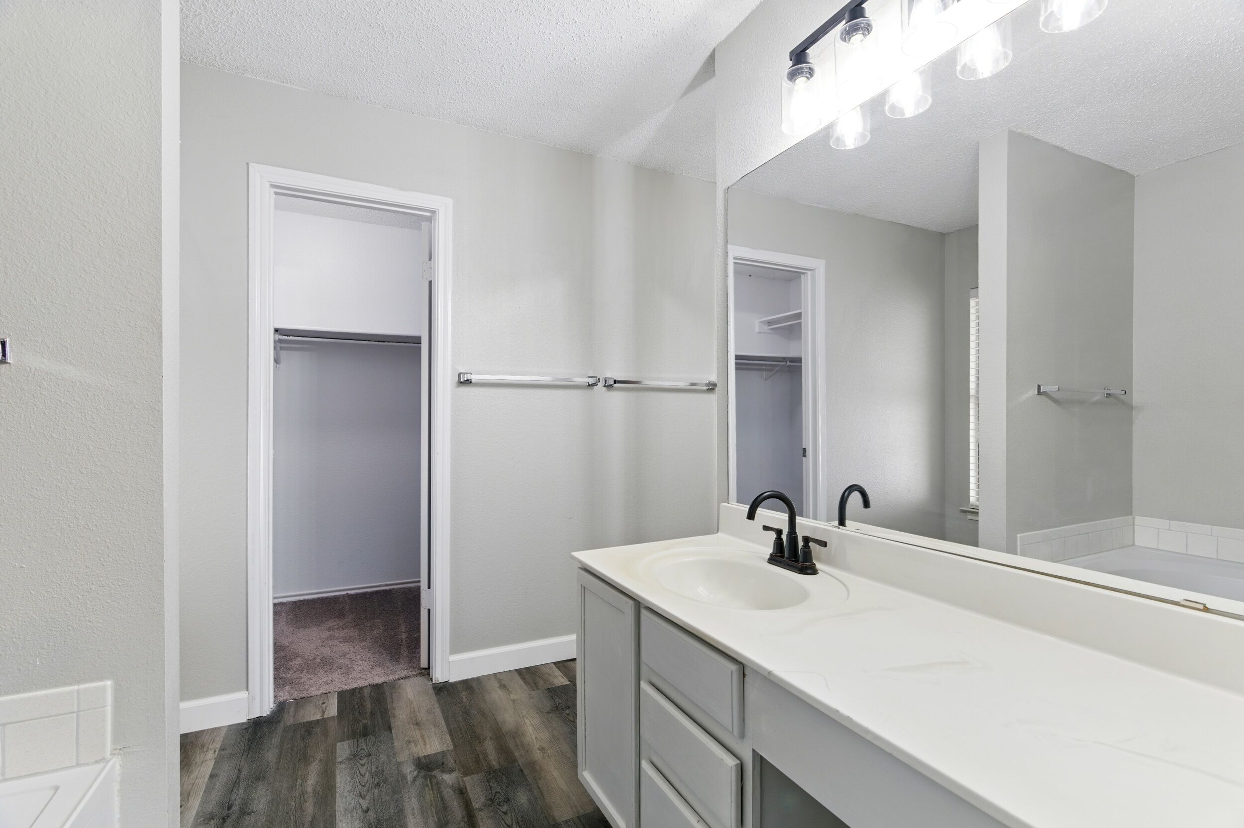 A bathroom with a white sink, black faucet, and a mirror with lights above.