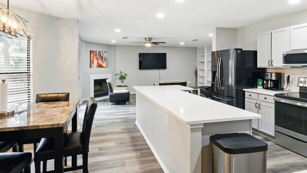 Una cocina moderna con muebles blancos, una isla central, electrodomésticos de acero inoxidable y un televisor de pantalla plana montado en la pared.