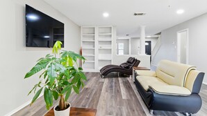 Una sala de estar moderna con televisor de pantalla plana, una planta grande, un sofá de cuero y estanterías empotradas.
