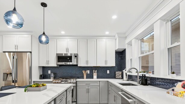 A modern kitchen with white cabinets, a stainless steel refrigerator, a microwave, and a wooden floor. - Somerville 4BR: 2 Parking/Yard/Game Rm—Near Boston (Somerville)