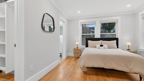 A bedroom with a bed, bedside lamps, a mirror, and a window with a view. - Somerville 4BR: 2 Parking/Yard/Game Rm—Near Boston (Somerville)