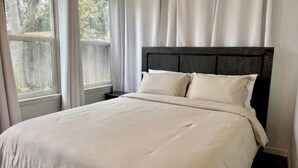 A neatly made bed with a dark headboard in a room with a large window and curtains.