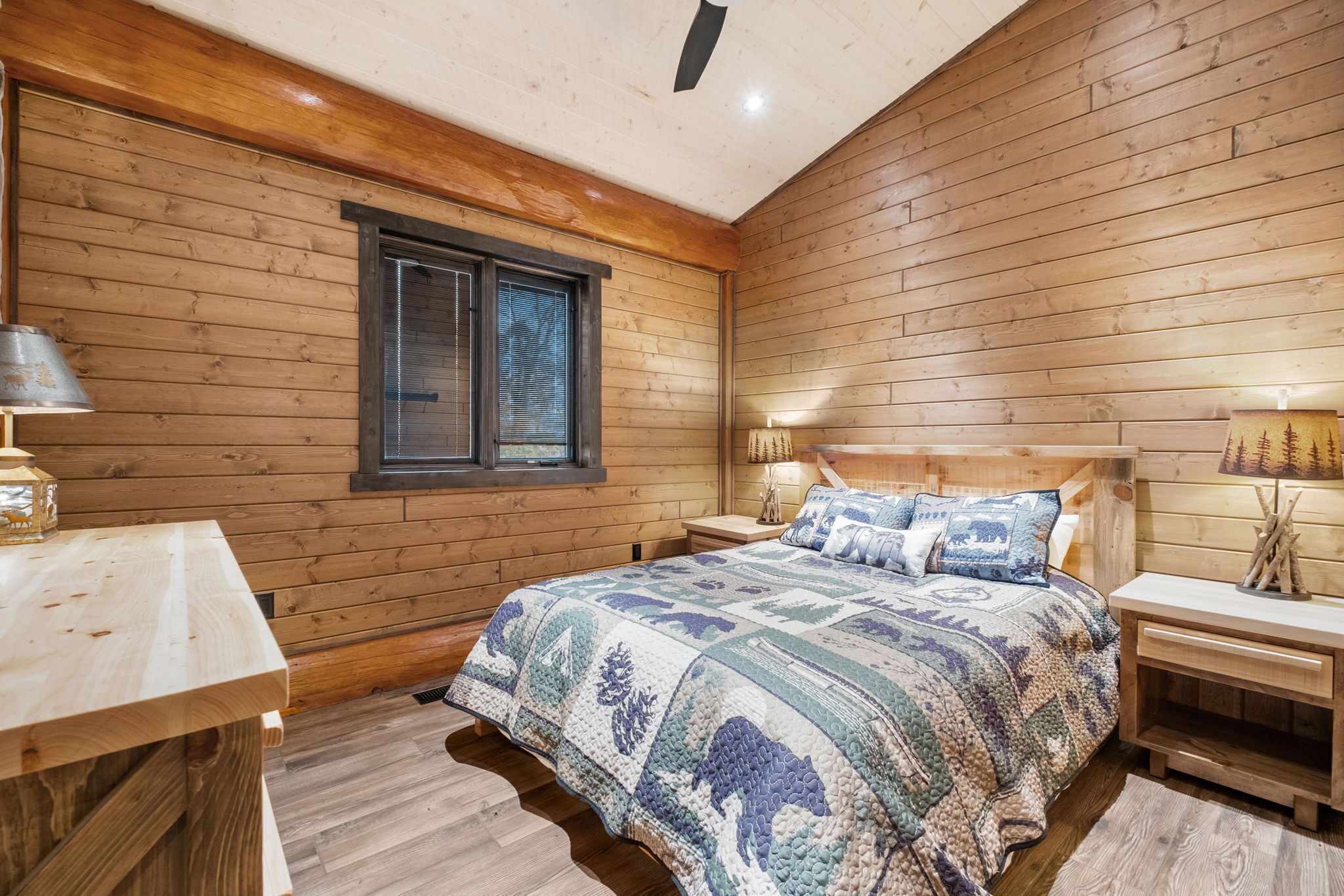 A cozy wooden cabin bedroom with a large bed, two bedside tables, and a window.