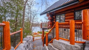 Una cabaña de troncos con una escalera de piedra que lleva a una terraza con mobiliario exterior.