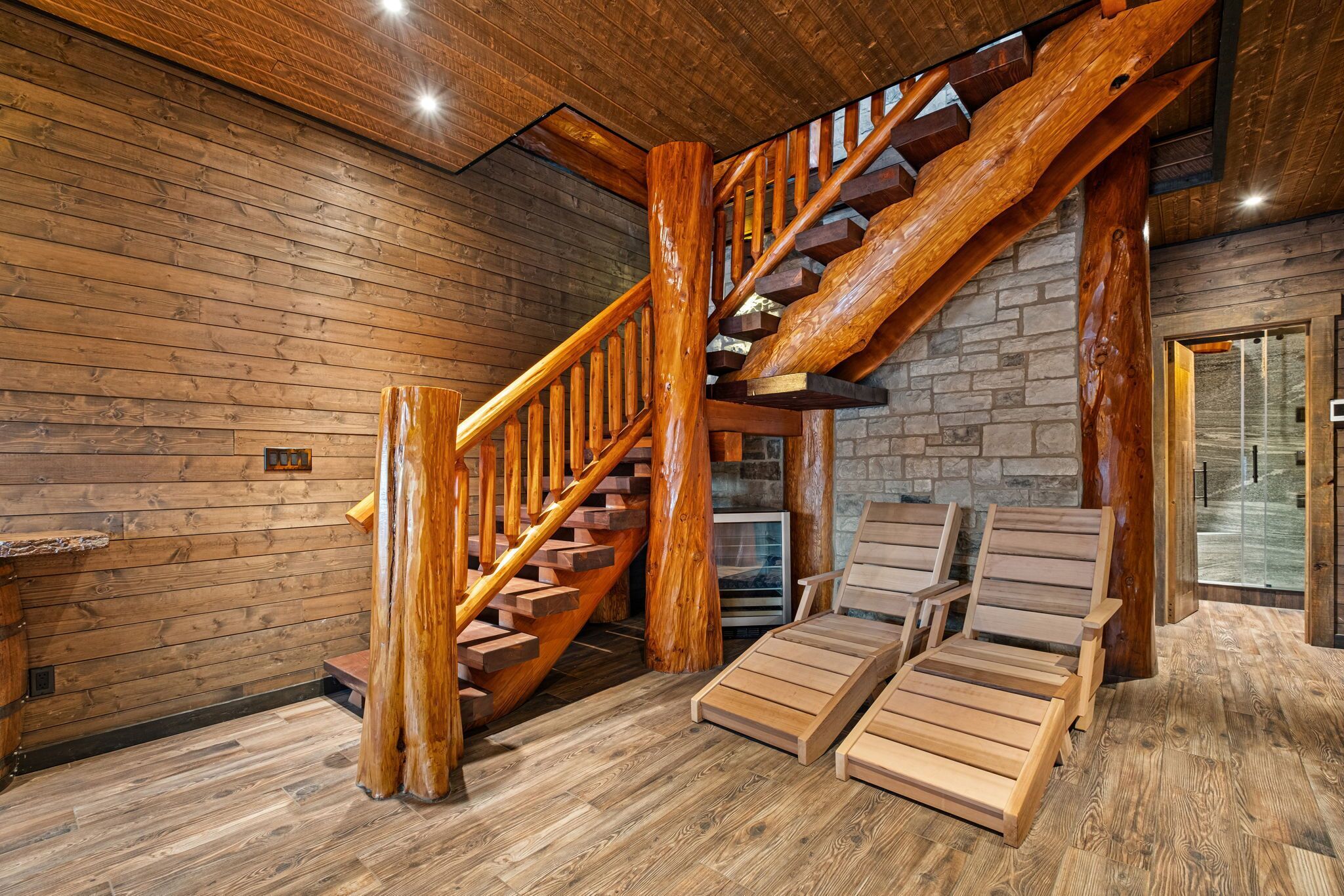 A wooden interior with a staircase, wooden flooring, and a glass door leading outside.