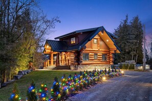 A log cabin with a stone foundation, wooden exterior, and a porch. - Luxury Waterfront Log Home with Hot Tub, Sauna & Game Room (Trent Hills)