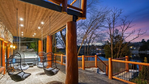 Una terraza de madera con sillones colgantes, un muro de piedra y vistas a un lago.
