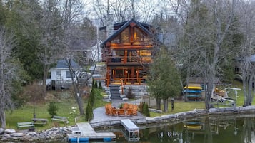 A lodge with a stone chimney, wooden deck, and a dock extending into a pond.