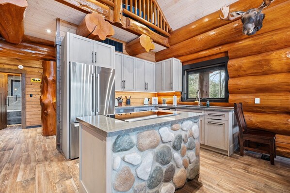 Une cuisine moderne dans une cabane en rondins, avec un îlot en pierre, des appareils en acier inoxydable et des éléments décoratifs en bois.