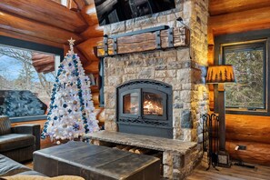 L’intérieur chaleureux d’un chalet avec une cheminée en pierre, un sapin de Noël blanc et un banc en bois brut.