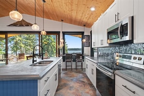 A modern kitchen with a large island, stainless steel appliances, and a view of the outdoors. - The Treasure Trove - A Dog-Friendly Waterview Gem (Grapeview)