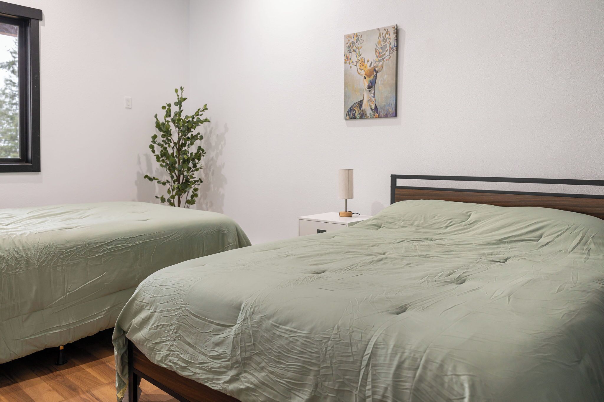 Une chambre avec deux lits, une table de chevet avec une lampe, un tableau accroché au mur et une fenêtre.