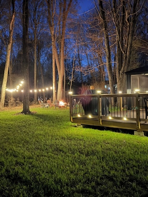 Eine Terrasse mit Lichterketten, umgeben von Bäumen und einer Rasenfläche.