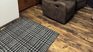 Un espacio habitable pequeño con kitchenette, un sofá de cuero marrón, un tapete estampado y una puerta con un cartel que dice 'Lost Cabin'.