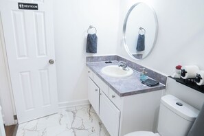 Et badeværelse med en hvid dør med teksten "RESTROOM", et marmortapet gulv, en hvid vask med sæbedispenser og et toilet.