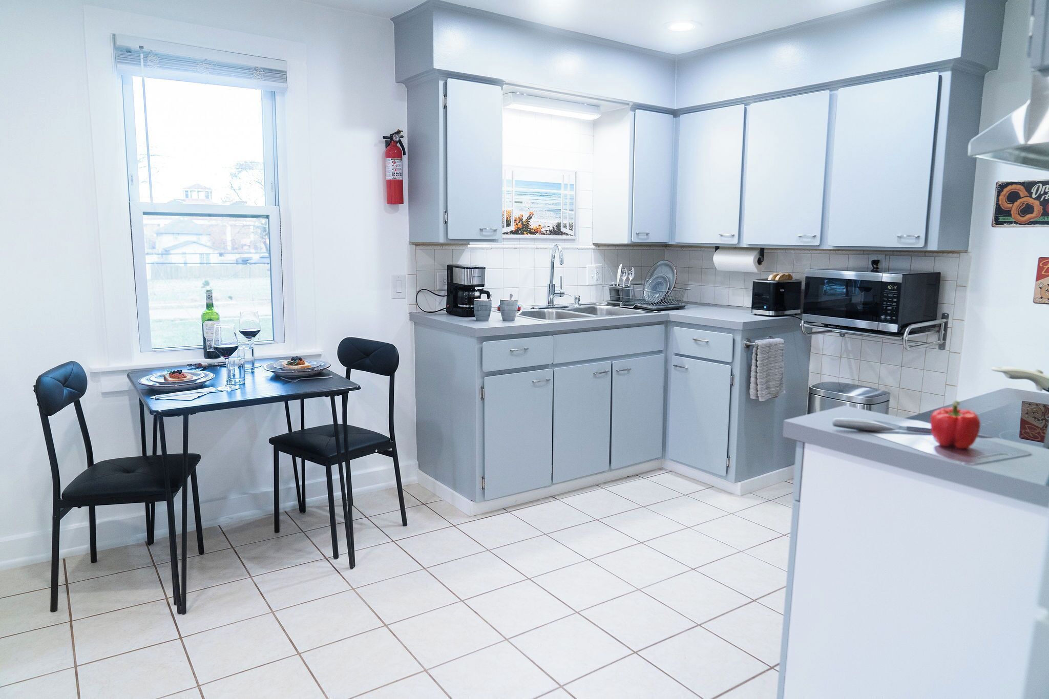 A modern kitchen with grey cabinets, a dining table with chairs, a coffee maker, a microwave, and a window with a view.