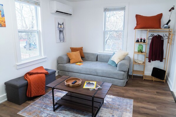 En stue med en grå sofa, et træ sofabord og en bænk med et orange tæppe.