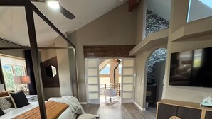 Une chambre à coucher avec un lit à baldaquin, un ventilateur de plafond, une grande fenêtre et une vue sur un mur en pierre.