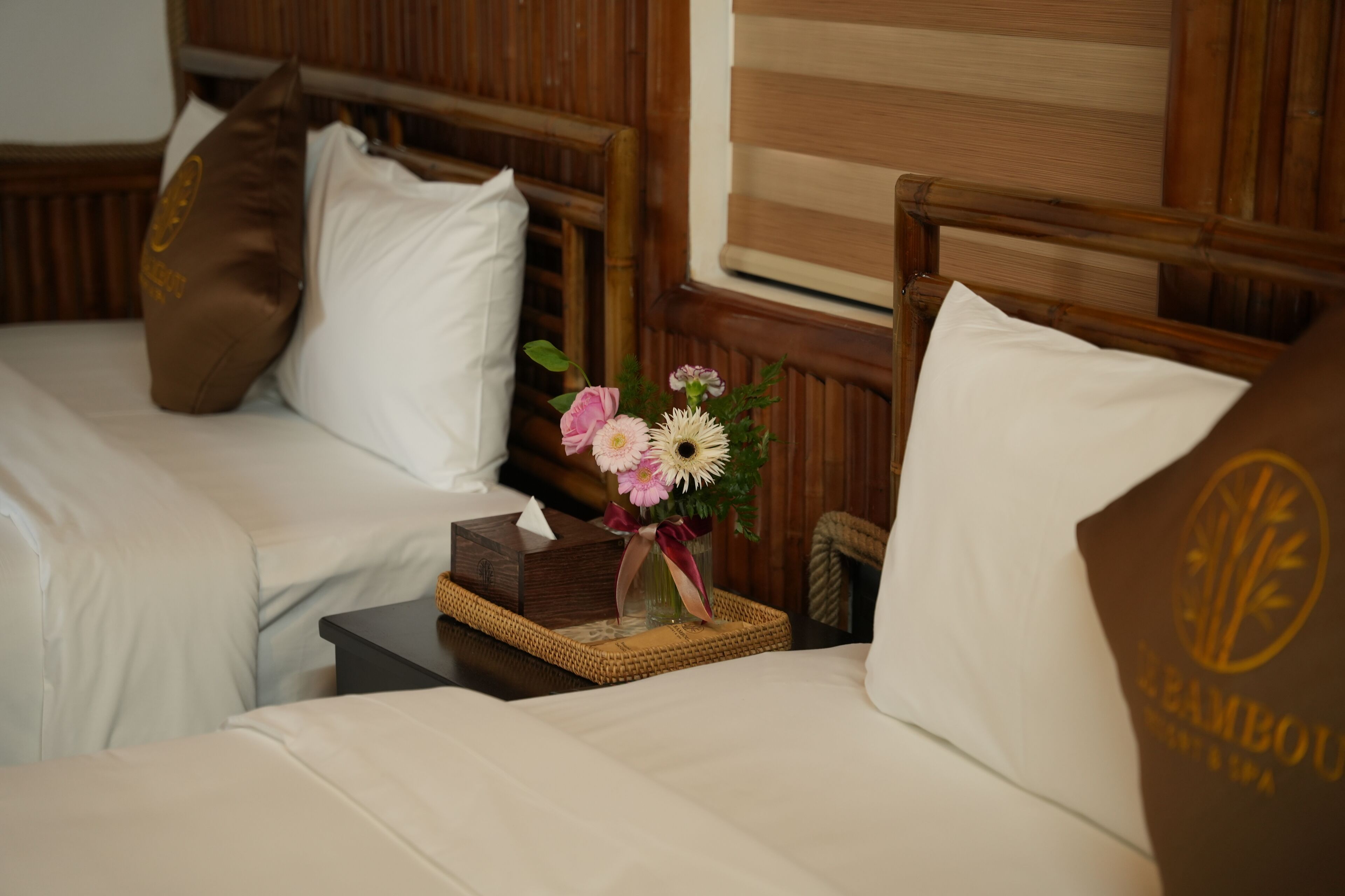 Habitación de hotel con dos camas, cabeceros de madera y una mesita de noche con un florero.