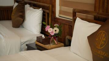 Habitación de hotel con dos camas, cabeceros de madera y una mesita de noche con un florero.